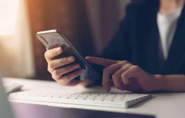 a person holding a phone and typing on a keyboard